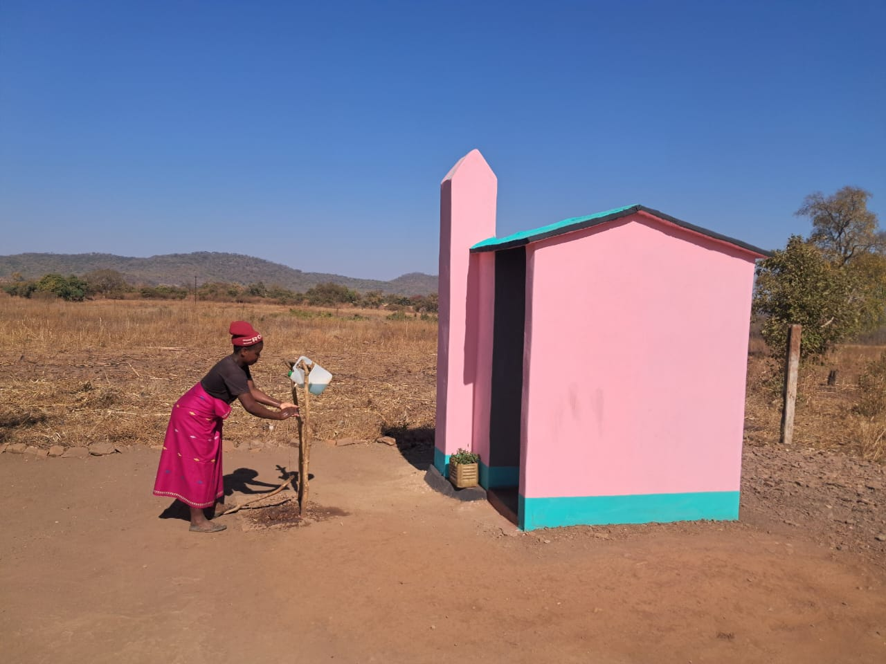 Resident washing hands beside a completed standard toilet at Mwemba Village Six